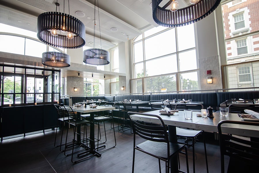 A restaurant interior without people, photographed on a sunny day, featuring high-top seating and dark blue banquettes.