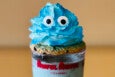 Blue whipped cream with candy googly eyes sits atop a cookie on a milkshake in a glass that says "Awful Awful - It's a drink."