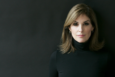 A headshot of a woman staring at the camera with a slight smile, wearing a black turtleneck against a dark background.