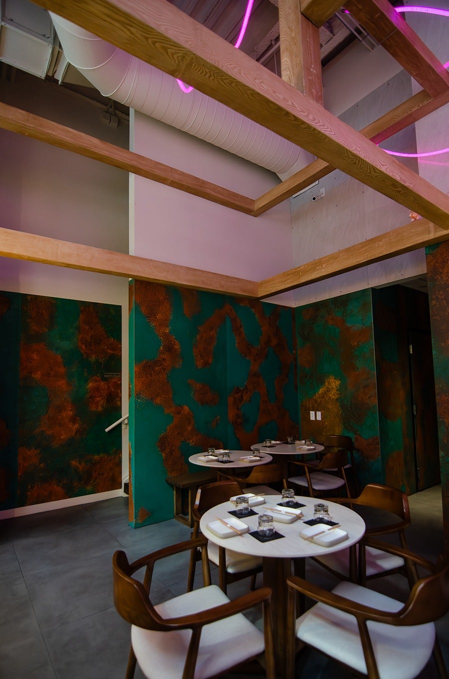 Restaurant interior featuring teal and bronze wallpaper, light wooden rafters, and a purple neon squiggle above the rafters.