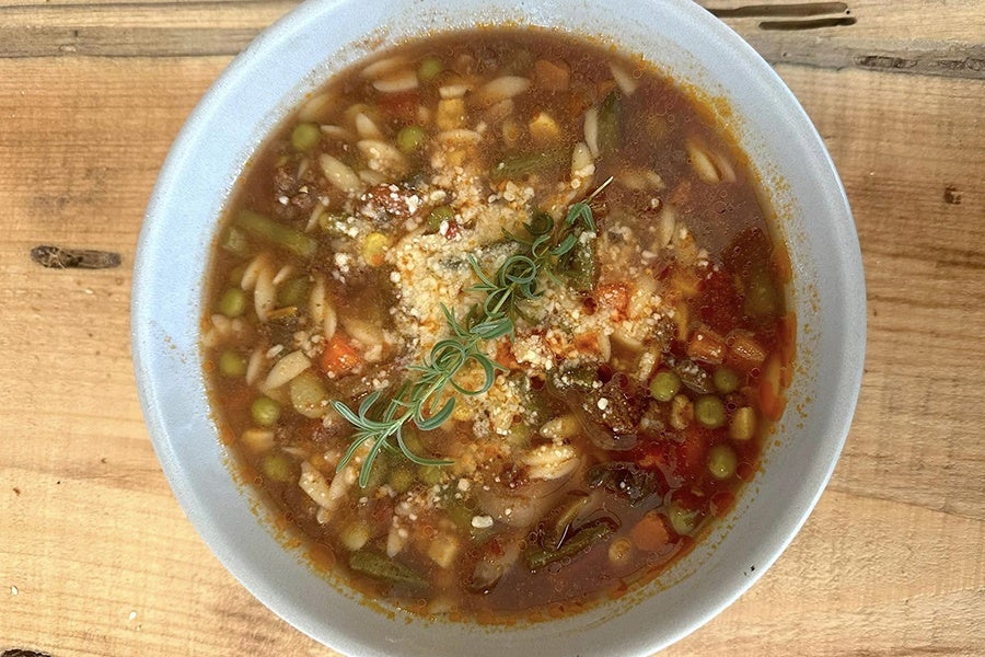 Overhead photo of a bowl of minestrone soup on a light wooden surface.