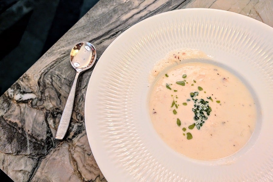 A bowl of chowder topped with chopped herbs on a black and white marble table.