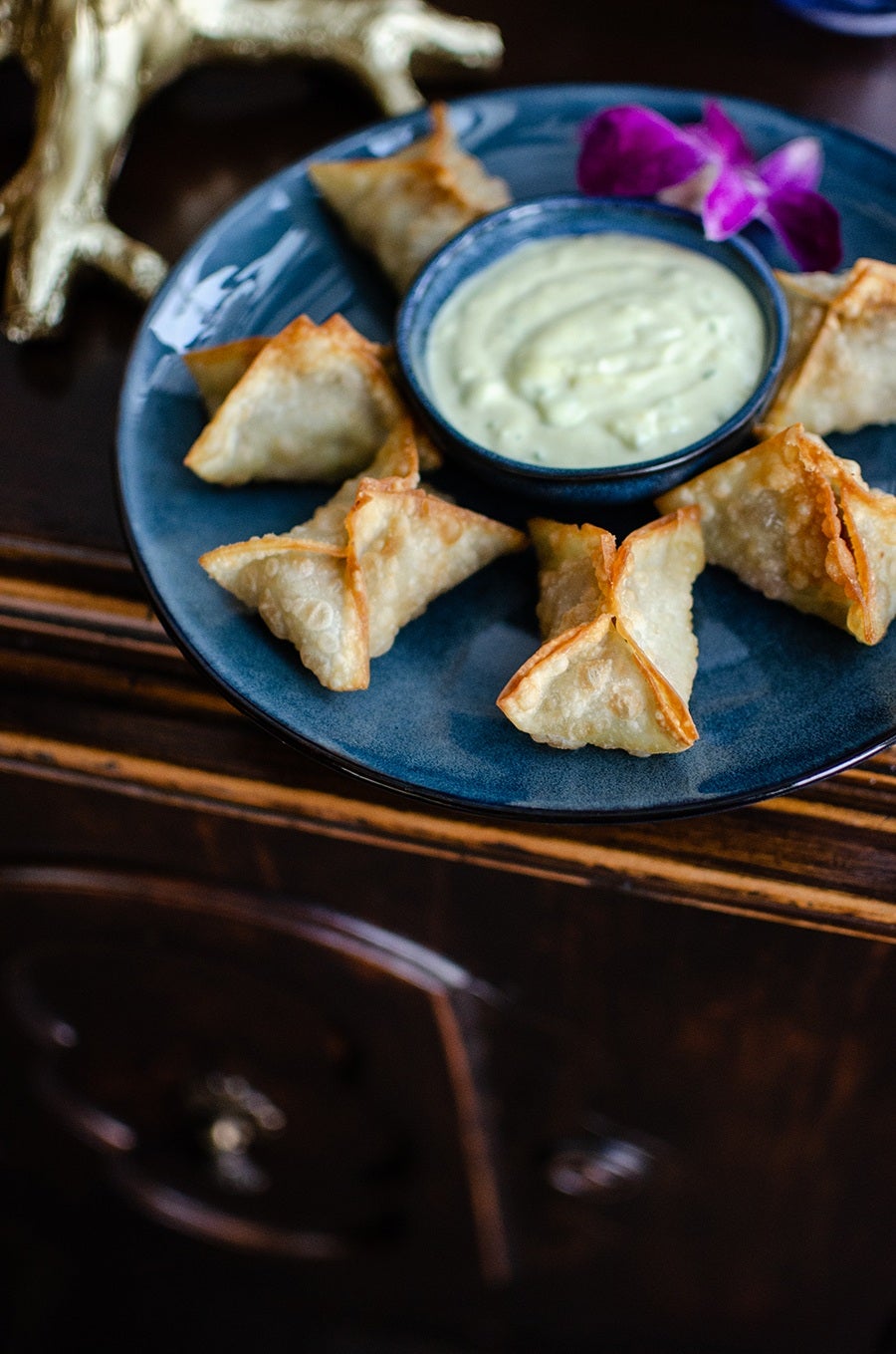 Fried wonton shells are folded into rectangles, displayed with an orchid and a creamy dipping sauce.