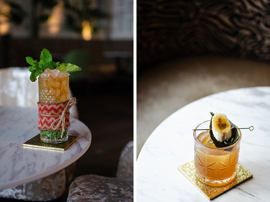 Two tropical cocktails. One is garnished with a lot of fresh mint, the other with a torched piece of banana.