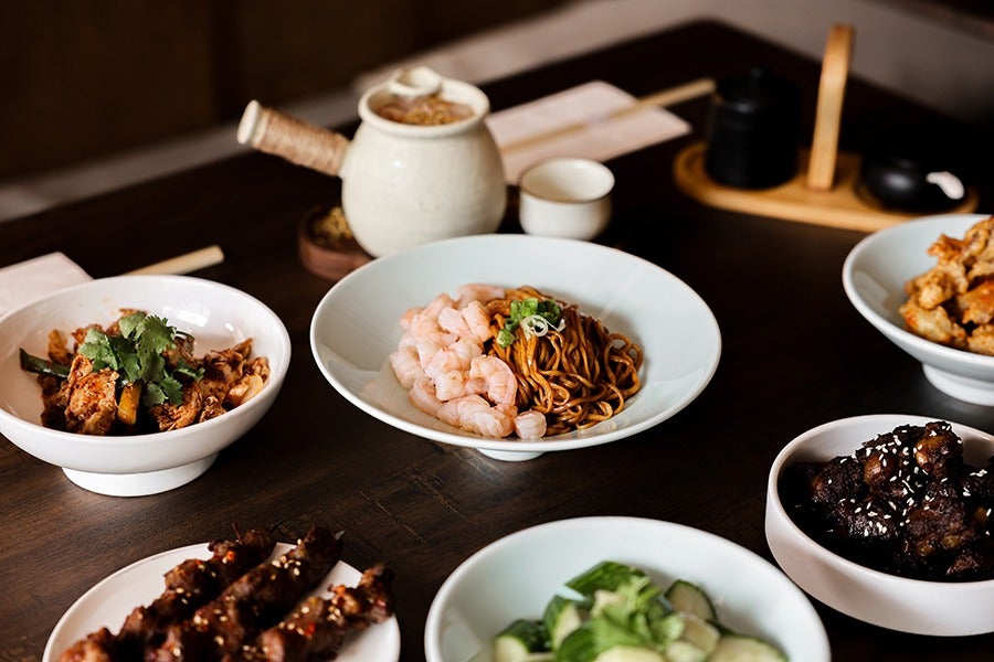 A tablescape of Chinese food, include a noodle dish with shrimp and a teapot.