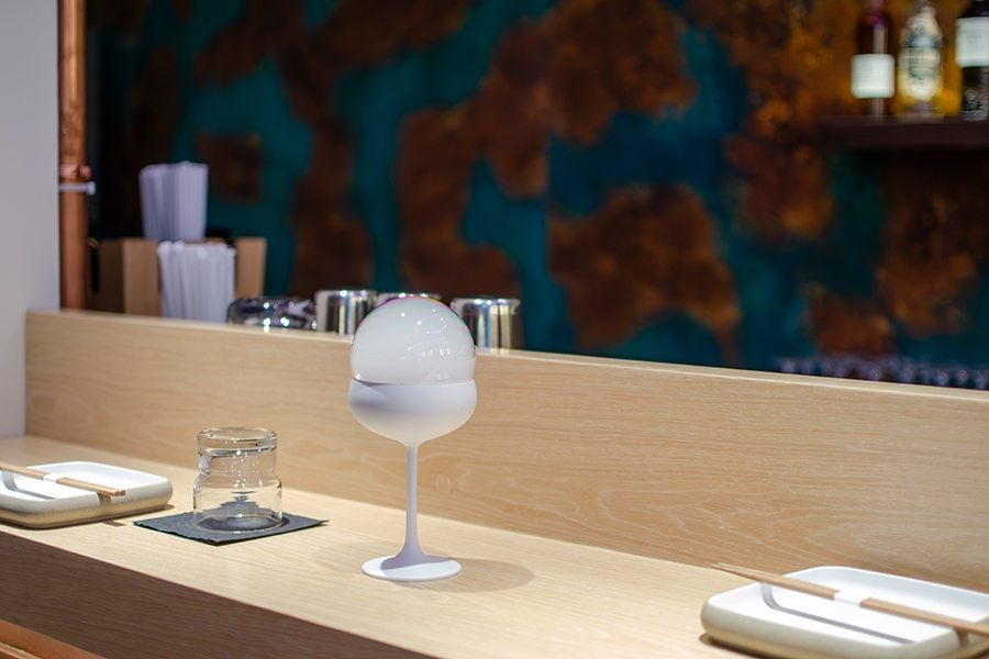 A cocktail sits on a light wooden bar with a bubble of smoke on it.