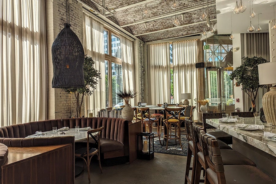 Empty restaurant interior during the day, featuring modern lightbulb light fixtures, long sheer-white curtains, and a half-circle brown banquette.