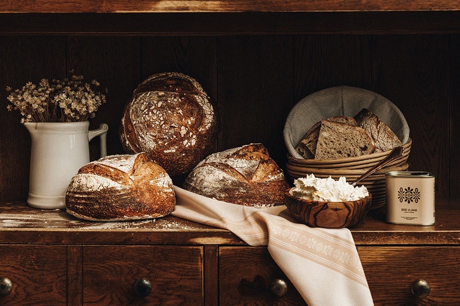 Loaves of sourdough bread are artfully arranged on a wooden shelf with a bowl of butter and a tin of olive oil.