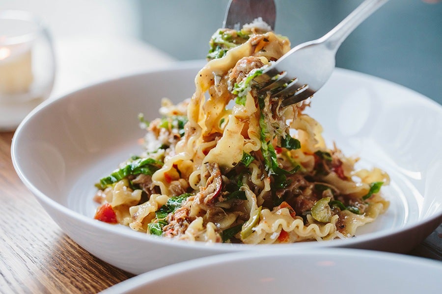 Two forks pull wavy pasta up off a plate.