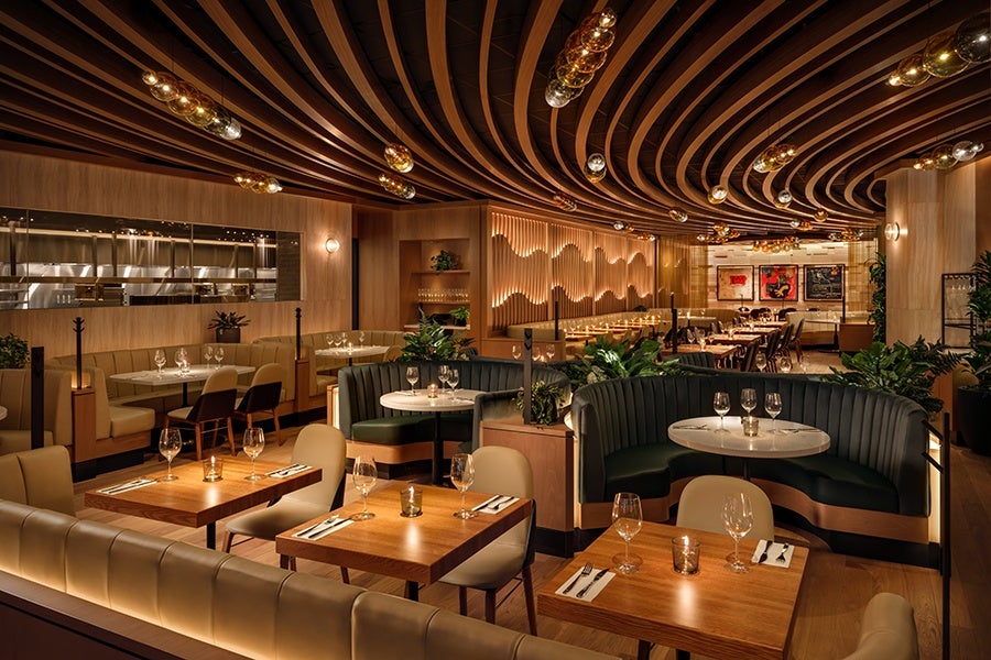 A restaurant dining room features a unique ceiling design of curved lines, deep green booths, and other elevated dining details.