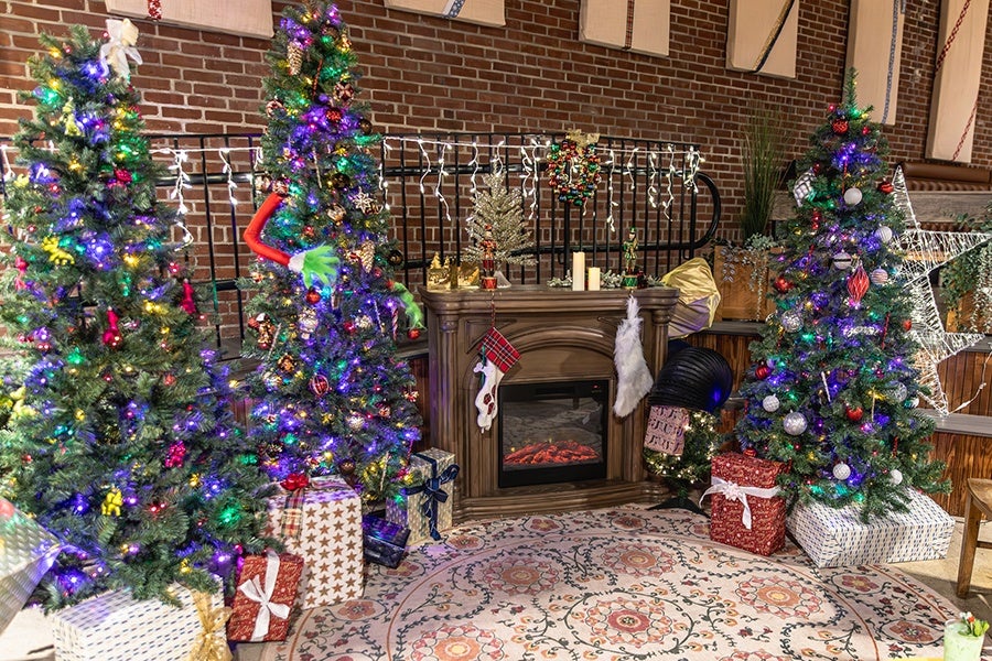 Christmas trees and presents surround a faux fireplace inside a bar.