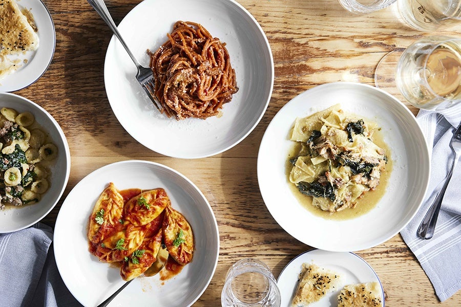 Overhead view of pasta dishes on a light wooden table.