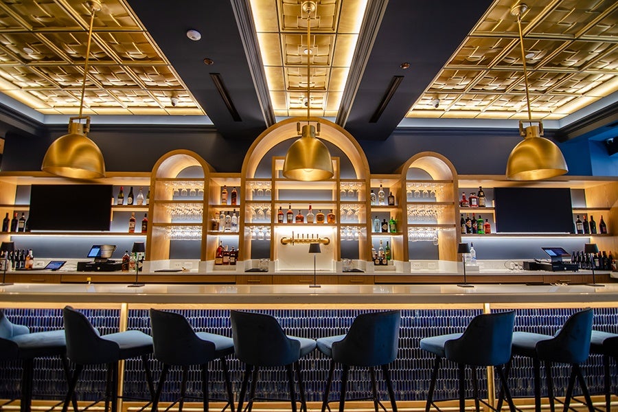 A bar area of a restaurant, empty of patrons, with dark blue, gold, and light wooden decor.