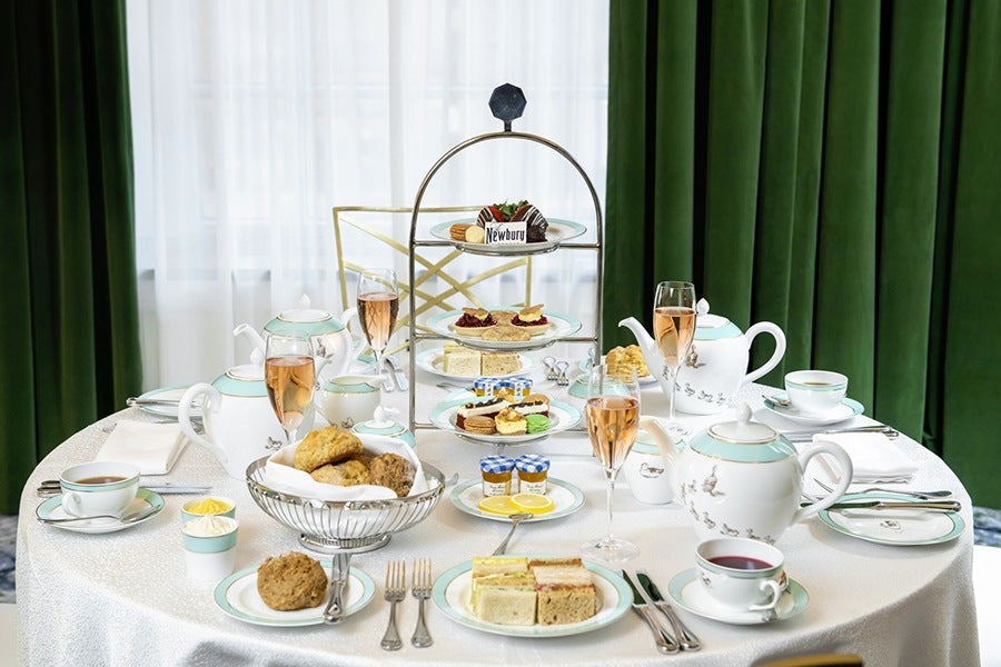 A fancy tea setup including a tower of mini sandwiches and treats. The teapots have ducklings on them.