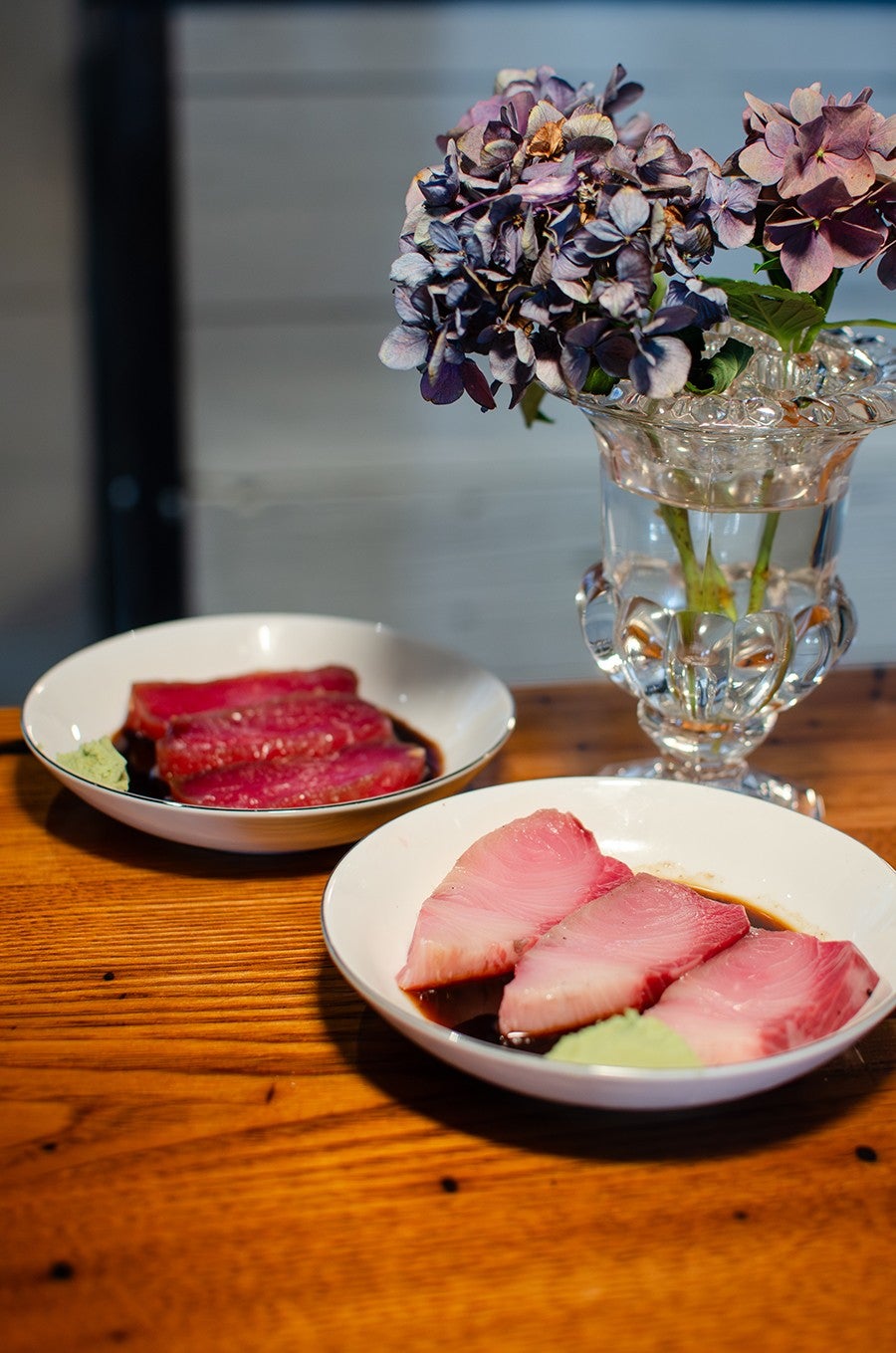 Two plates of sashimi - three plump slices each - in a pool of soy sauce with a bit of green wasabi.