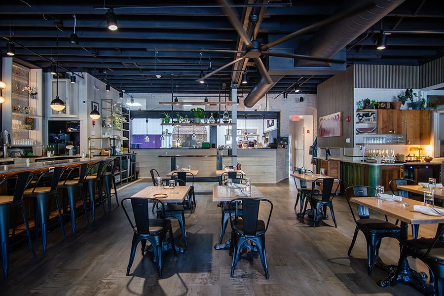 A restaurant interior without people in it. The vibe is neighborhood-y, with lots of light wood surfaces, pops of color, and plants.