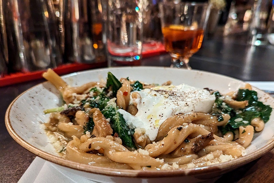 Twists of pasta with greens and burrata on a bar.