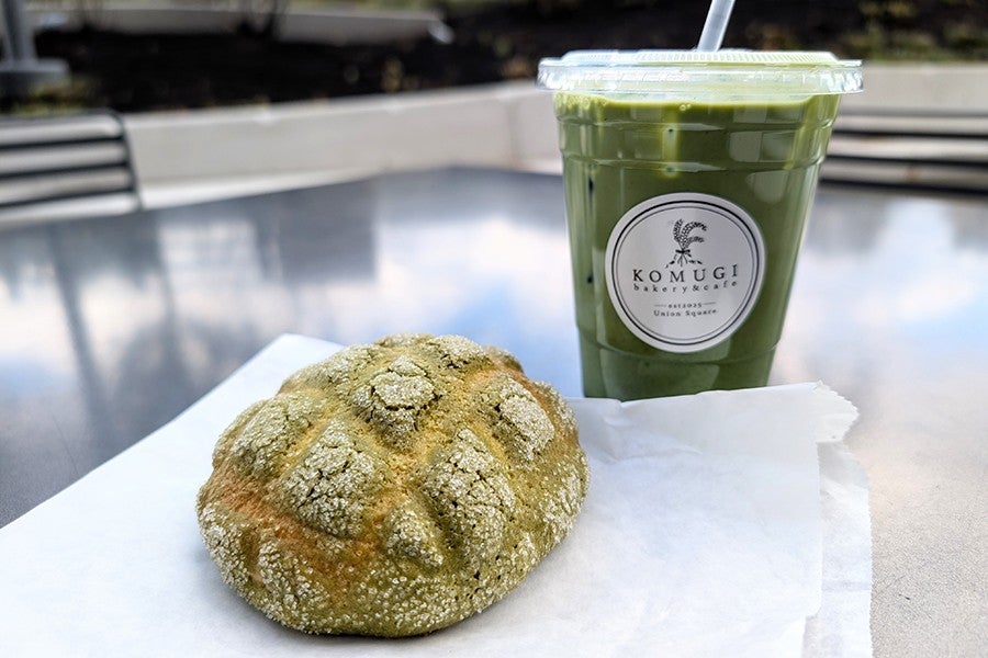 A green Japanese pastry bun is accompanied by a green iced drink on an outdoor table.