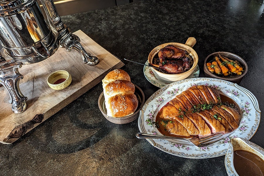 Various duck preparations on a counter next to a shiny silver duck press.