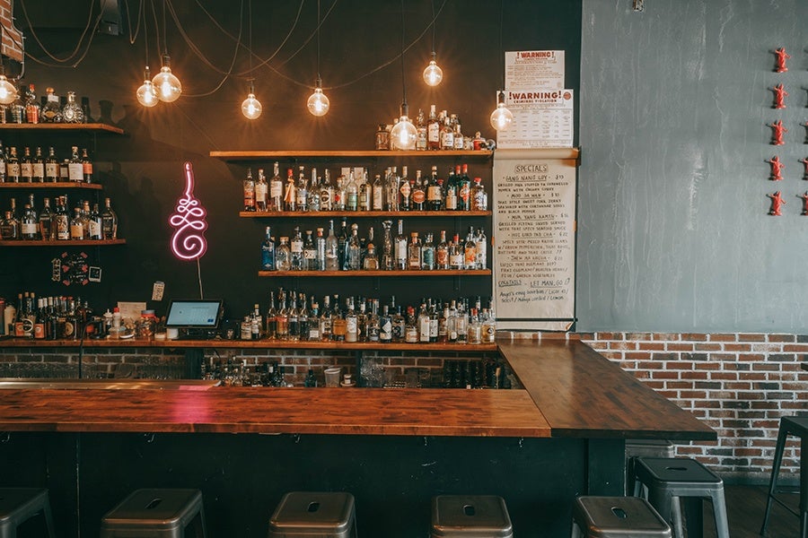 The bar area in a Thai restaurant, featuring exposed brick, dark wood, and a pink neon symbol.