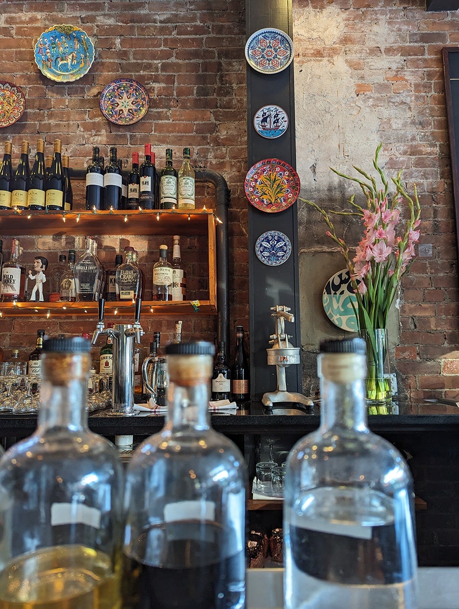 The backbar at a restaurant features weathered brick and colorful decorative plates.