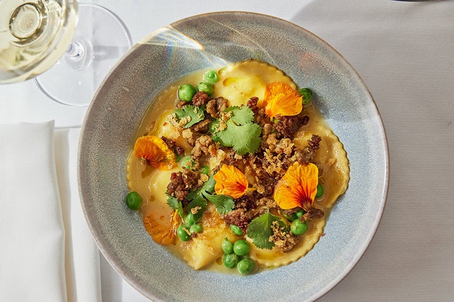 Overhead view of an elegant plate of ravioli with peas and edible flowers.