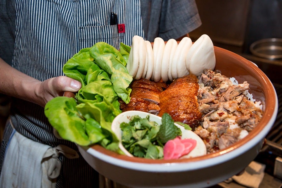 A chef's hands hold a plate of roasted duck with lettuce, bao, and other accoutrements.