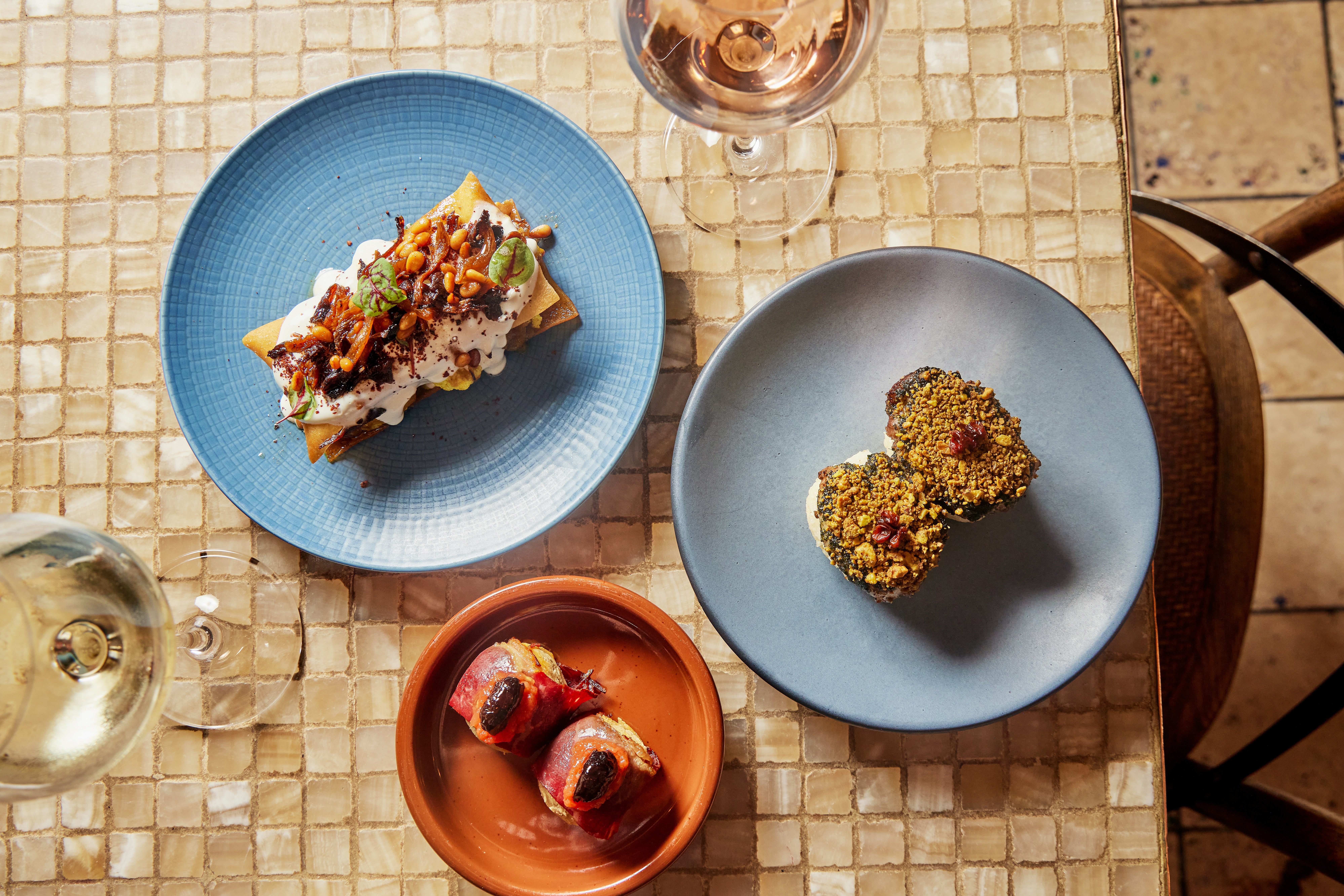 Overhead view of three Mediterranean dishes on an off-white tiled table.