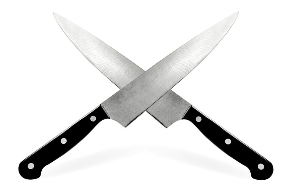 Two chef knives with black handles crossed over each other on a white background.