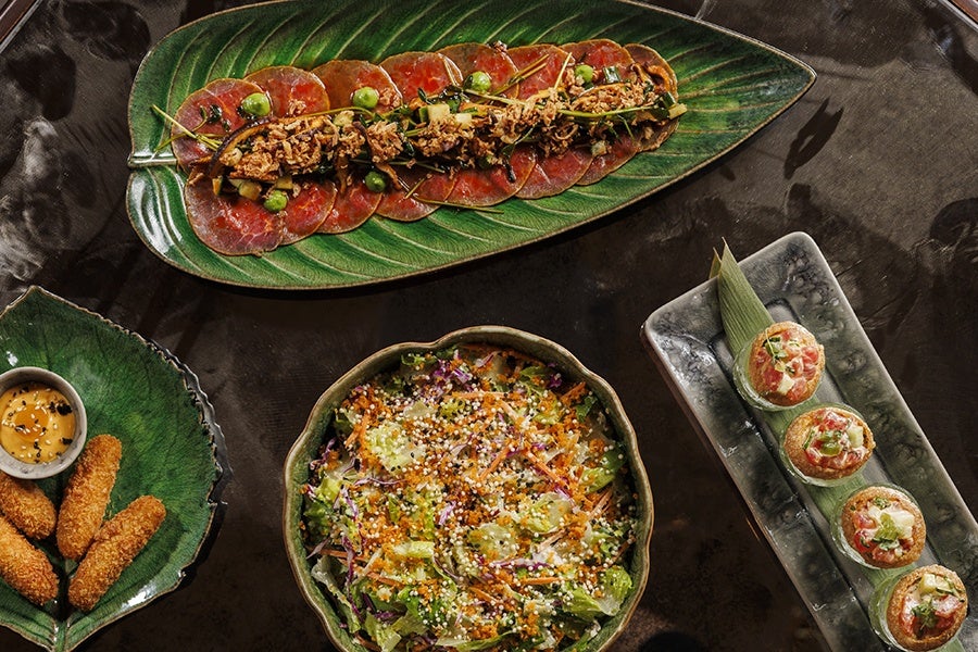 Overhead view of a salad, beef carpaccio, and other dishes on a dark table.