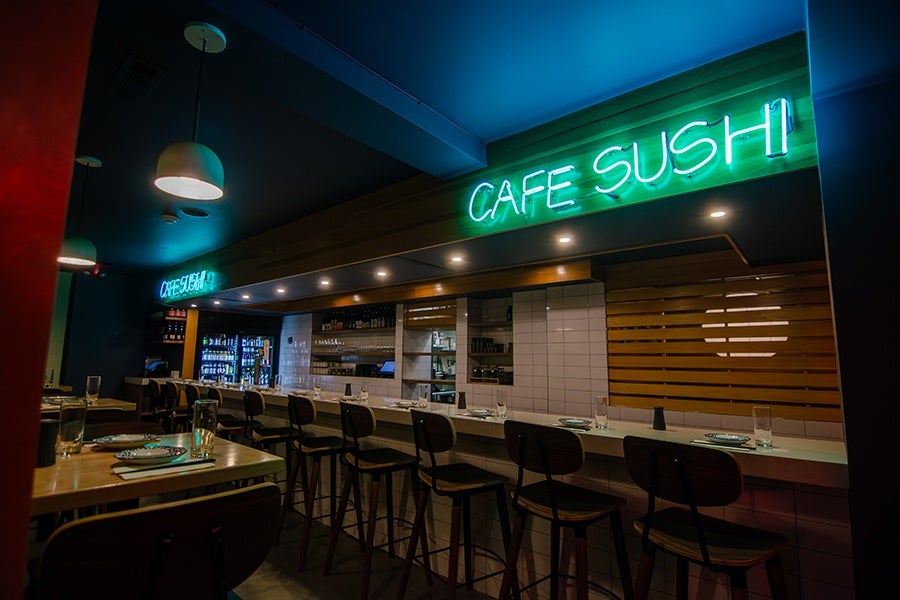 A bar in a Japanese restaurant is adorned with two blue neon signs reading Cafe Sushi.