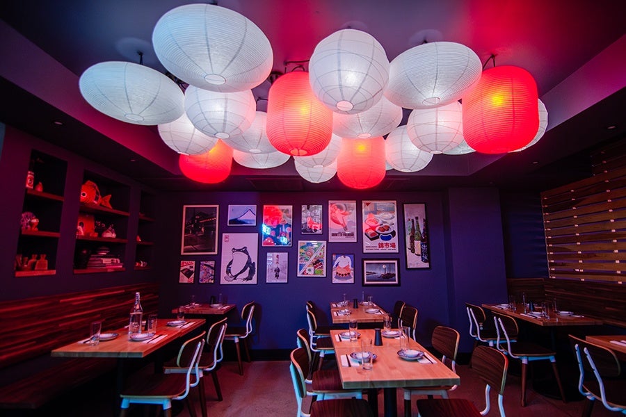 A Japanese restaurant's dining room features red and white paper lanterns hanging from the ceiling and dark blue walls.
