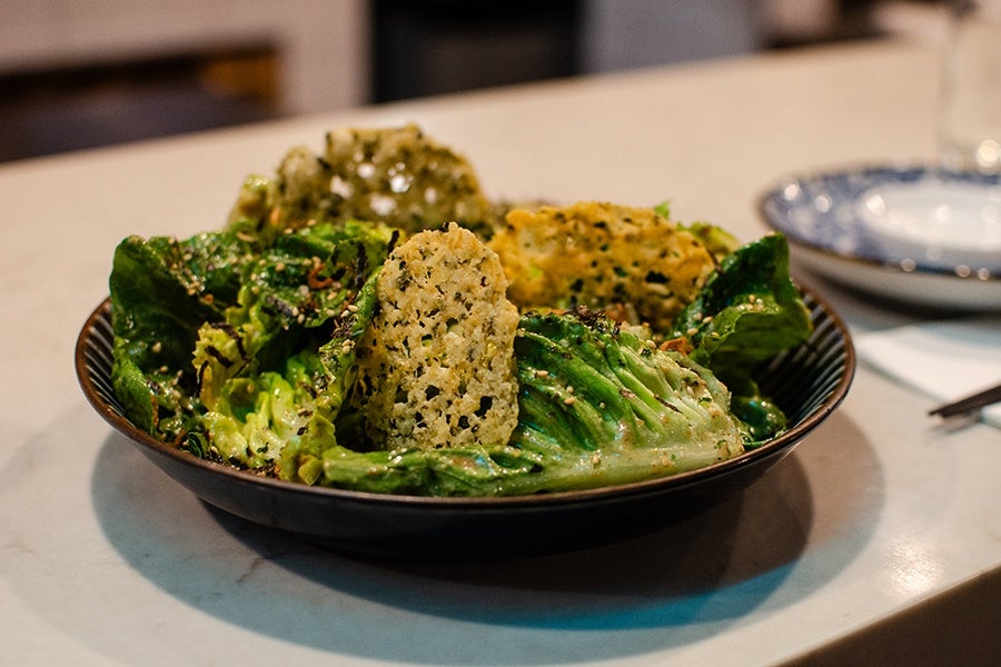Dressed greens are garnished with big, herby parmesan crisps in a bowl.