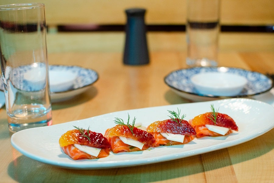 Four pieces of raw salmon are lined up on a plate, garnished with wedges of blood orange and bits of fennel and dill.