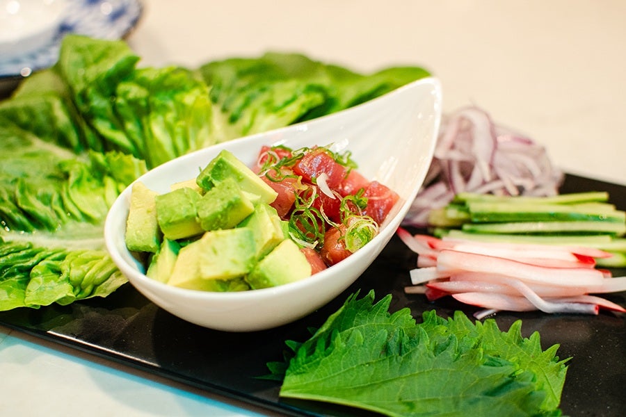 Cubes of tuna and avocado sit in a teardrop-shaped plate on a platter of lettuce leaves and sliced cucumbers, onions, and other veggies.