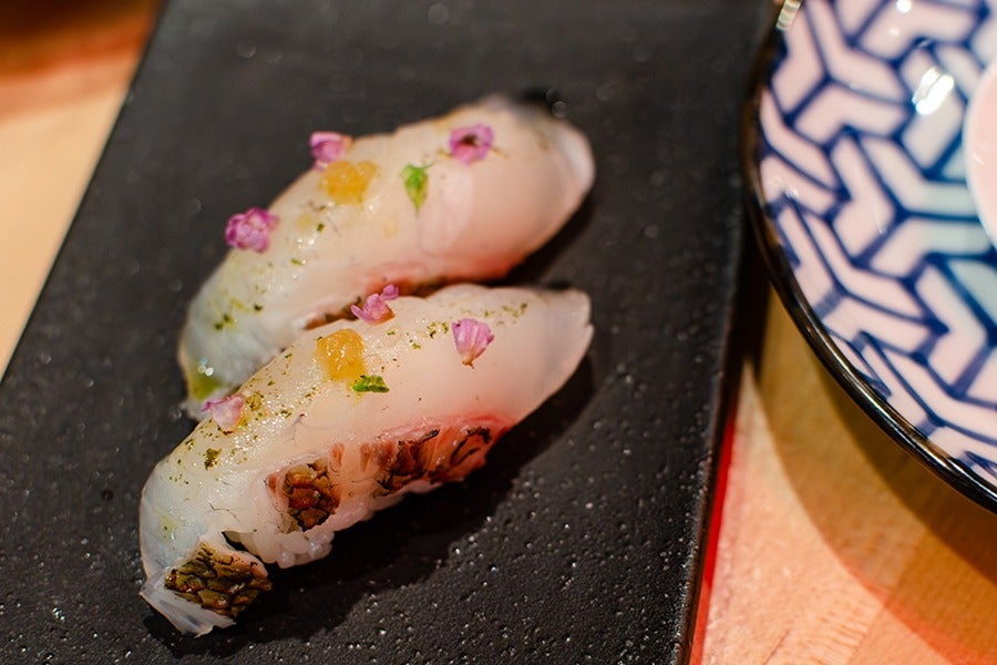 Two pieces of white nigiri are topped with bits of purple flower and other garnishes.