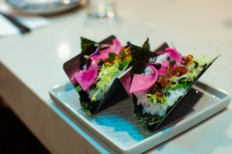 Two sushi handrolls stuffed with rice, ikura, and more sit in a taco holder.