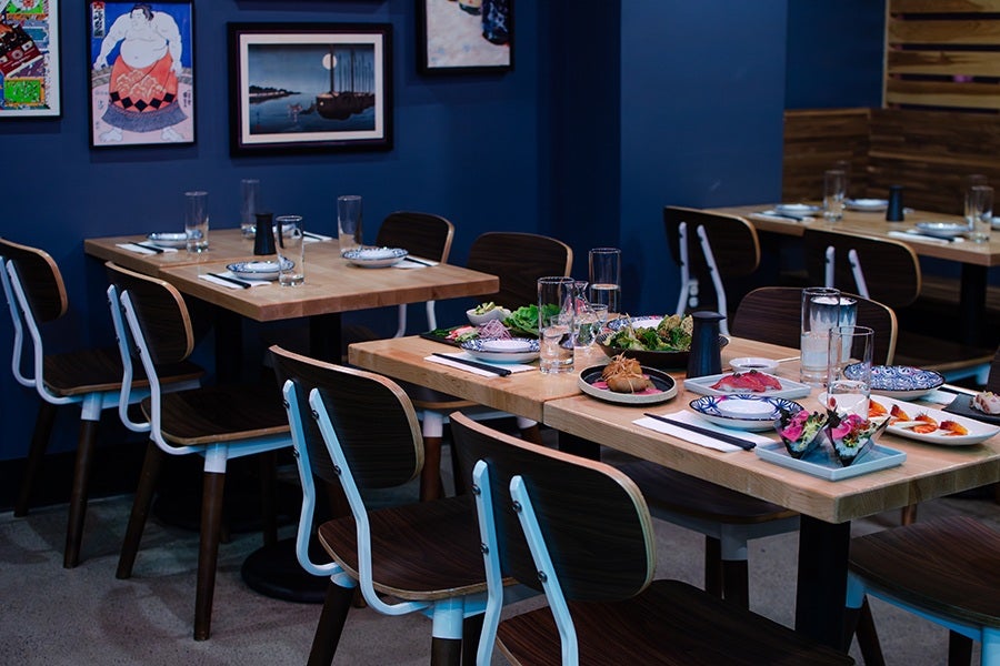 A Japanese restaurant dining room with dark blue walls and a table full of sushi and small plates.
