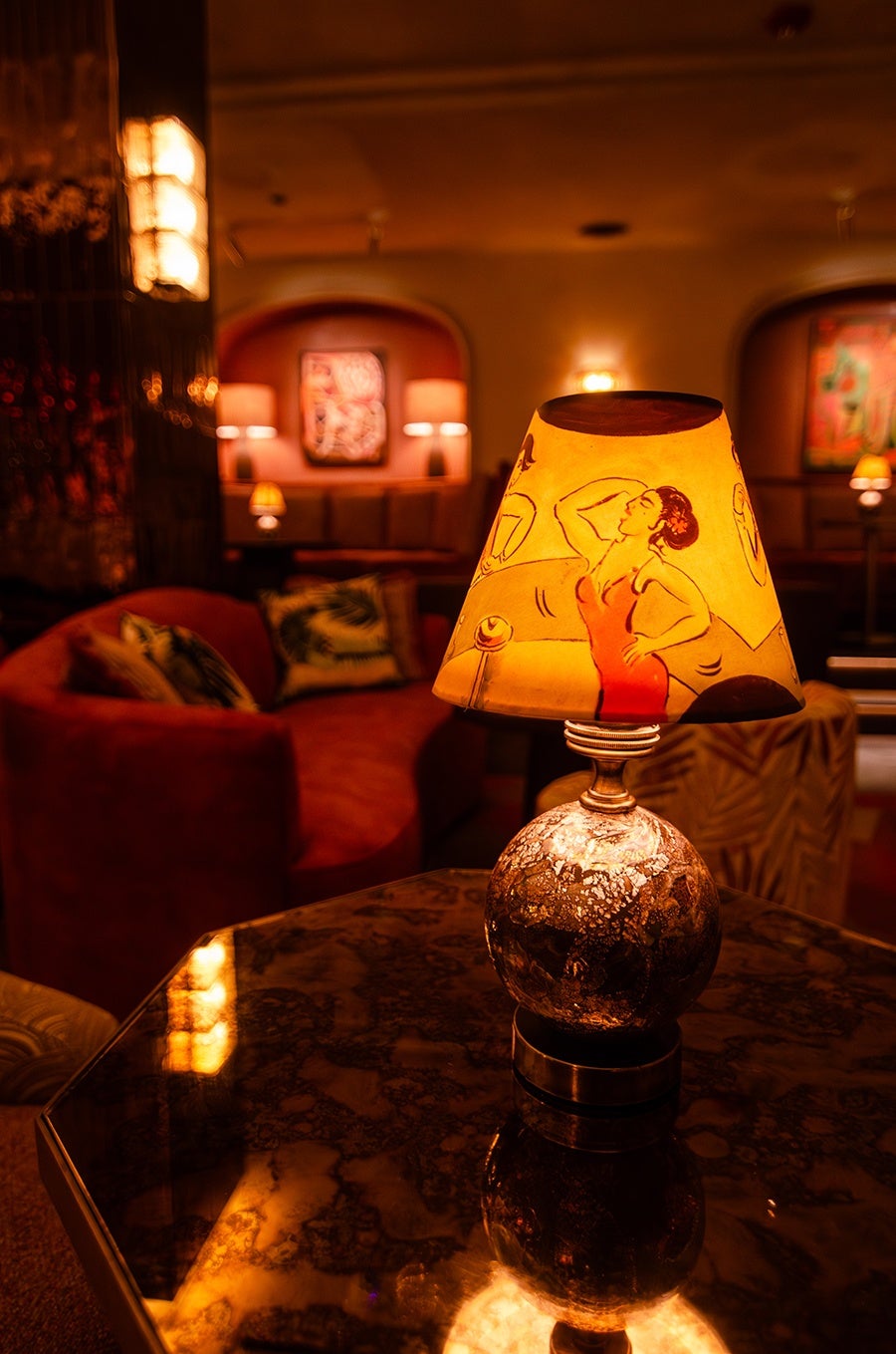 Closeup on a lamp at an upscale cocktail lounge, with a woman in a red dress painted on the lampshade.