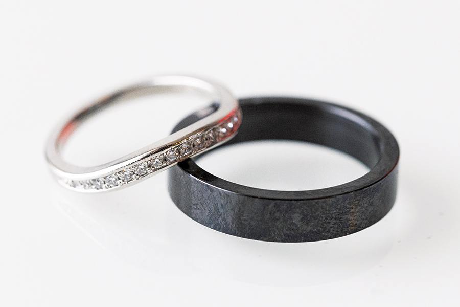 Two rings placed on a white surface: one is a thin silver band with small diamonds embedded along the top, and the other is a thicker, plain black band with a matte finish.