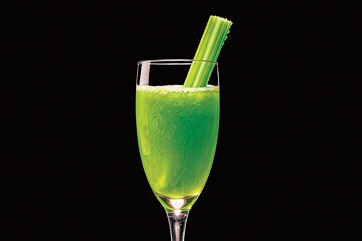 Tall clear glass filled with a frothy green juice, garnished with a stalk of celery, set against a black background.