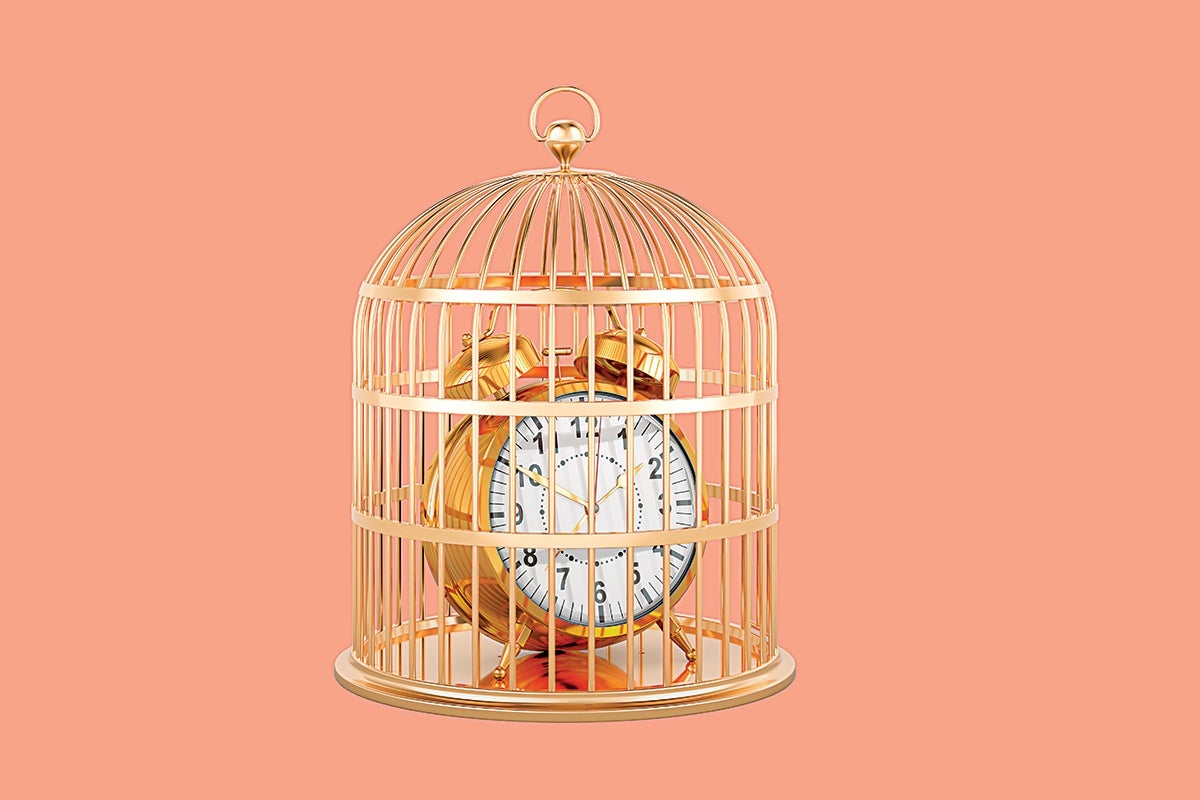 A gold-colored vintage alarm clock enclosed inside a matching gold birdcage, set against a solid peach background. The clock face is white with black numbers and gold hands.