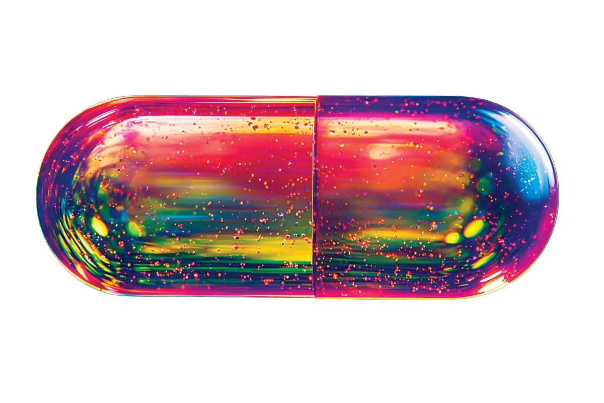 A large, glossy capsule-shaped object with a vibrant, multicolored surface featuring shades of pink, red, yellow, green, and blue. The capsule has a shiny, reflective texture with small specks of glitter-like particles scattered throughout. The background is plain white.