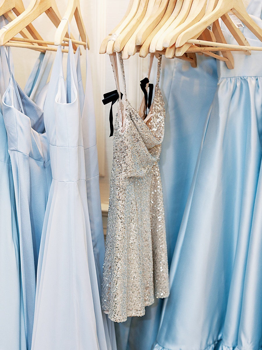 Light blue and silver sequin dresses hanging on wooden hangers, with the silver dresses featuring thin straps and black ribbon details.