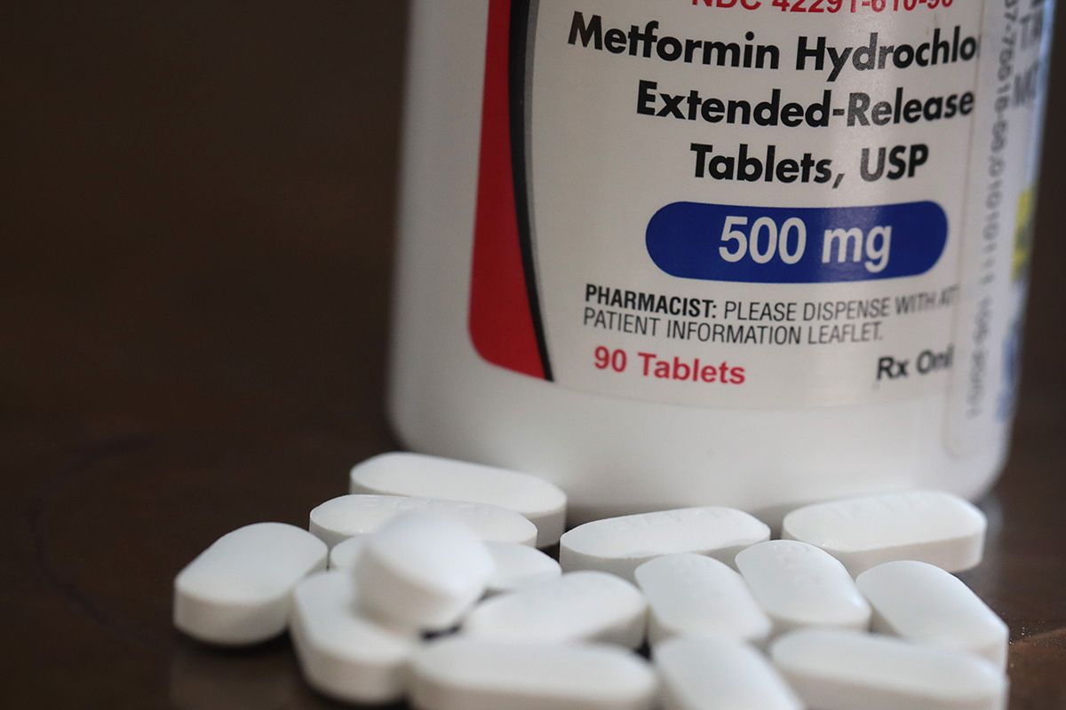 White oblong tablets scattered in front of a bottle labeled "Metformin Hydrochloride Extended-Release Tablets, USP 500 mg," containing 90 tablets.