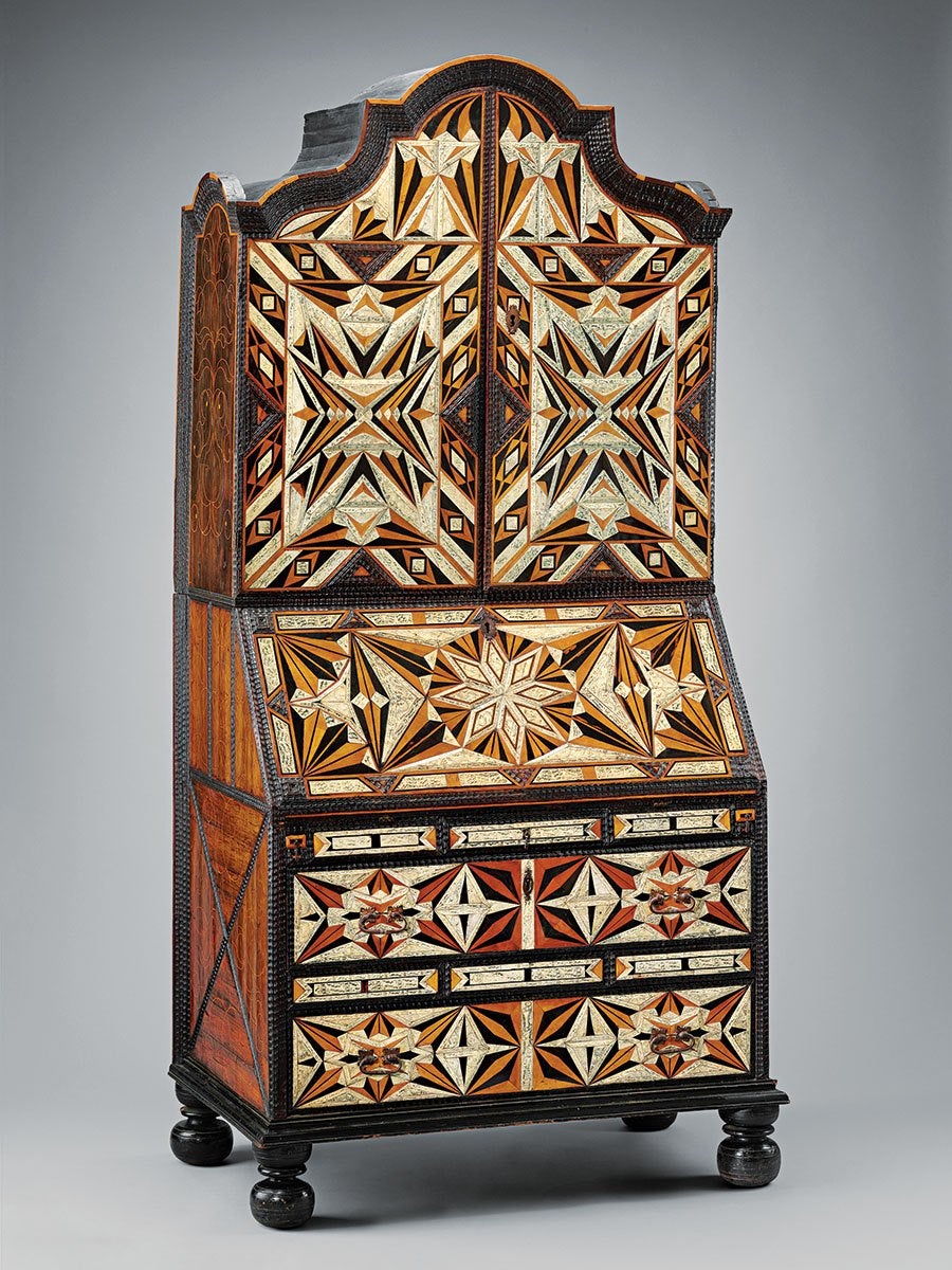 A tall wooden cabinet with intricate geometric inlay patterns in shades of black, white, orange, and brown. The cabinet has a curved top section with two doors, a slanted middle section with a starburst design, and two drawers at the bottom featuring symmetrical star and diamond motifs. The piece stands on four rounded black feet.