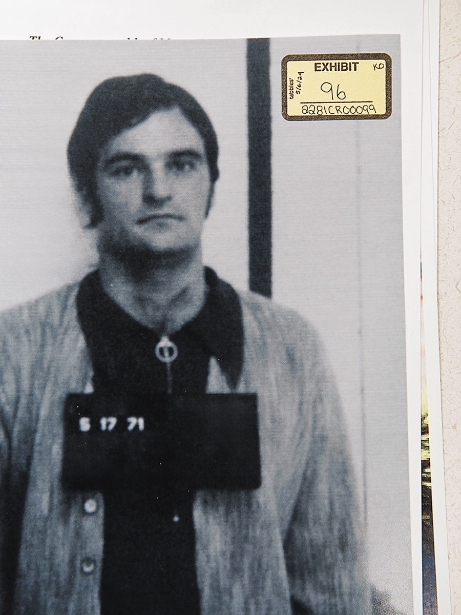 Black and white mugshot photograph of a man with dark hair wearing a cardigan over a dark shirt, holding a placard with the date "5 17 71." The photo has an "EXHIBIT 96" label in the top right corner with additional handwritten notes.
