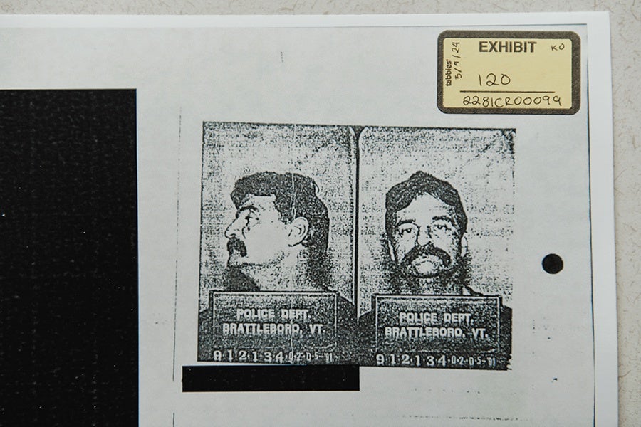 Black and white photocopy of a mugshot showing two views of a man with dark hair and a mustache, one profile and one frontal. The placard in the photos reads "POLICE DEPT BRATTLEBORO, VT" with a number below it. The photocopy is labeled as "EXHIBIT 120" with additional handwritten notes and a hole punch on the right side.