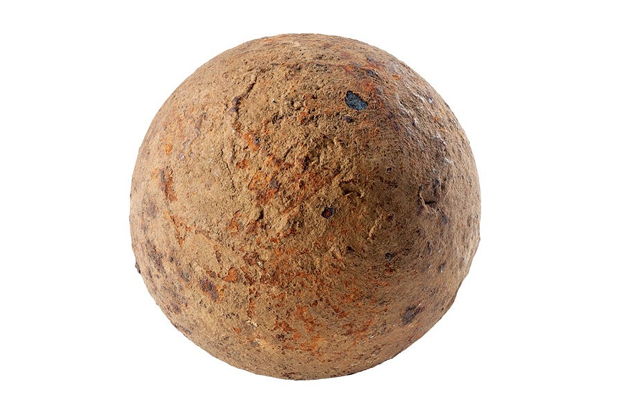 A spherical object with a rough, rusty, and weathered surface texture, predominantly brown with patches of orange and dark spots. The surface appears uneven and corroded, resembling an old iron cannonball or a heavily rusted metal sphere.