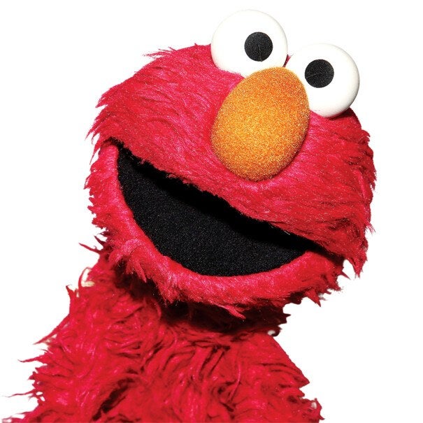 Red furry puppet with large white eyes and black pupils, an orange oval nose, and a wide open black mouth, tilted slightly to the side.